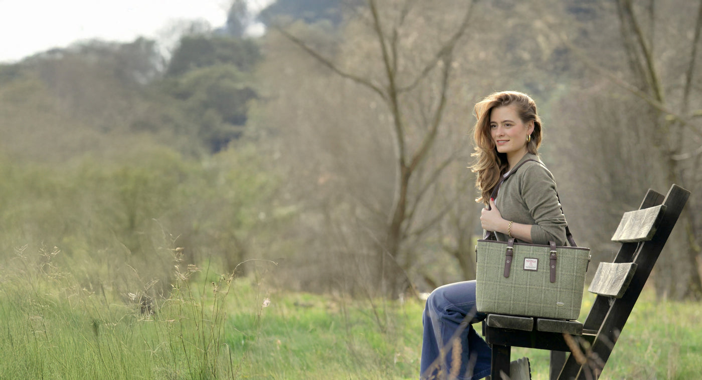 Woman sitting on a bench in a natural setting with a green bag.
