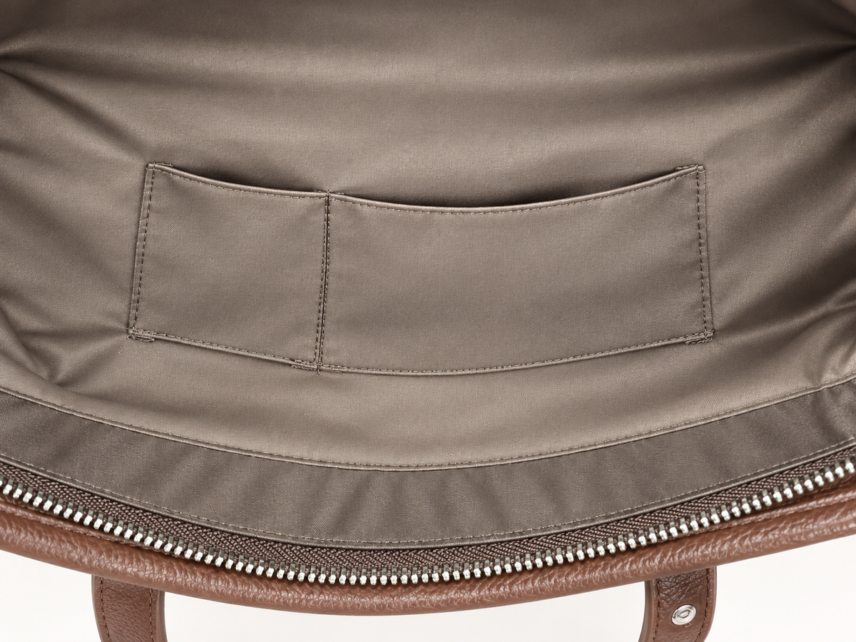 Close-up of the interior lining of a brown leather bag, showing a taupe fabric pocket and silver zipper.