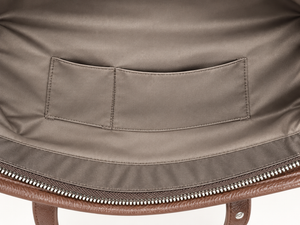 Close-up of the interior lining of a brown leather bag, showing a taupe fabric pocket and silver zipper.